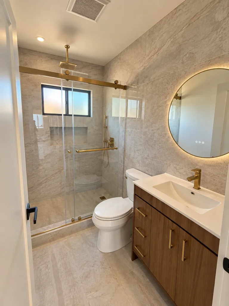 Bathroom in the Encino remodel, glass shower and a round lit mirror